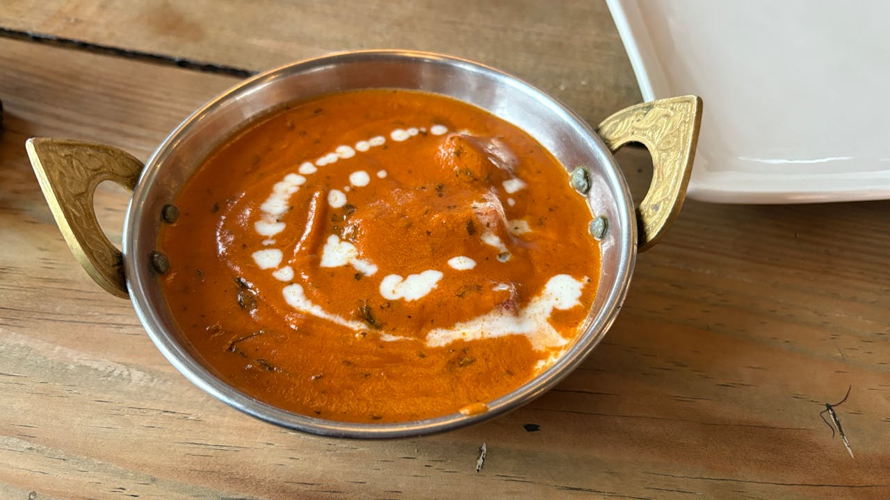 our-services-1 Authentic Indian butter chicken served in a brass bowl with creamy sauce, on a wooden table.